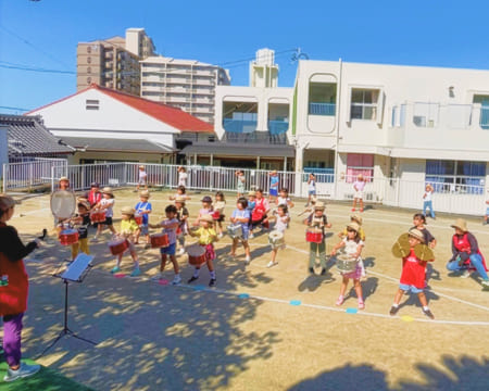 園庭で太鼓やシンバルなどの楽器を持って演奏する様子