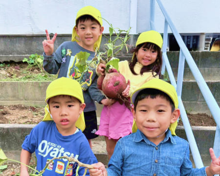 秋の遠足で掘った大きなサツマイモを誇らしげに見せている様子