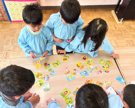 机の上に広げたカードでゲームをしている園児たちの様子