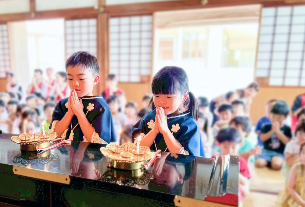 お寺の本堂で行事に参加し、手を合わせてお参りをする園児たち