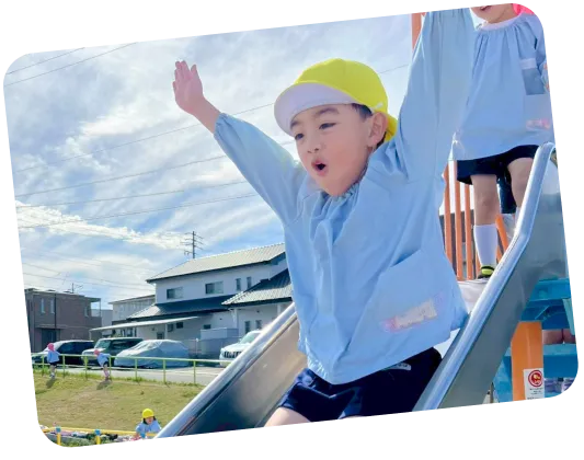 青空の下で両手を広げて滑り台を滑り降りる元気な男の子