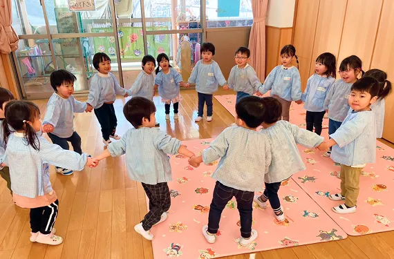 お部屋の中で手をつなぎ大きな円を作って遊ぶ園児たち